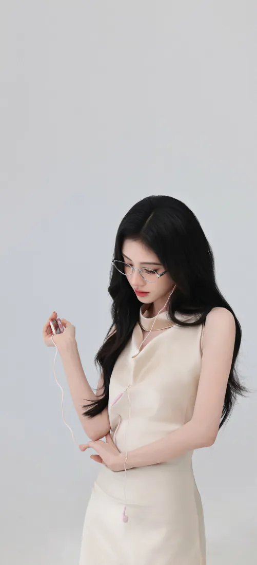 鞠婧祎着米白无袖长裙戴细框眼镜，在浅灰棚拍背景前低头垂眸。