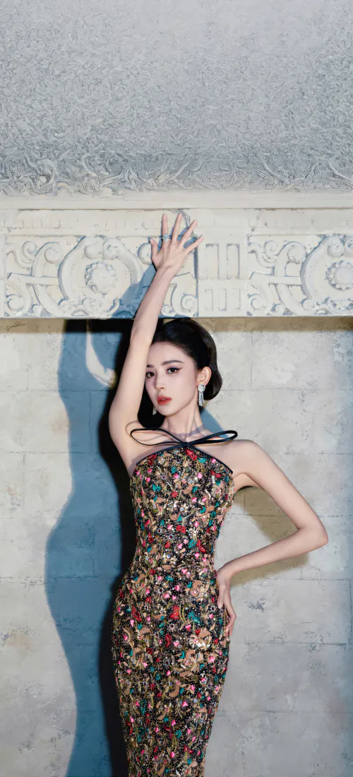 古力娜扎身着碎花挂脖修身礼服，盘发造型，倚靠墙边抬手，姿态优雅复古。