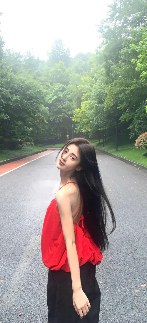 穿红色吊带的长发女子站在林间湿滑步道上回头望向镜头，背景是茂密绿树。