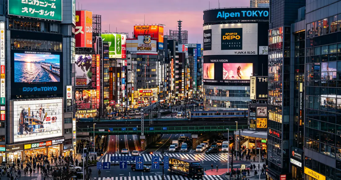 黄昏时分东京新宿繁华街景，高楼林立布满霓虹招牌，路口行人车辆穿梭。