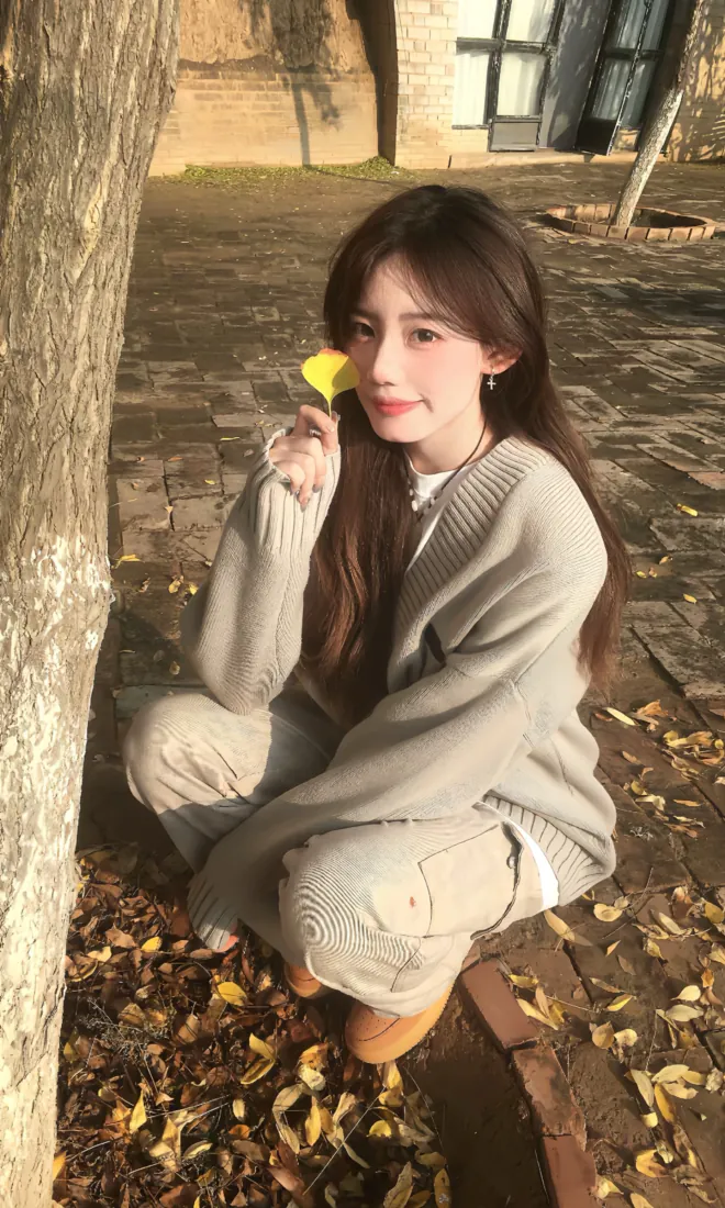 长发少女蹲在铺满银杏落叶的庭院砖地上，手持黄叶，暖调秋日氛围。