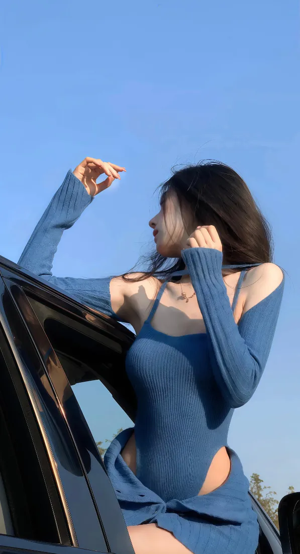 低角度仰拍蓝衣长发美女倚在黑色车边，背景是澄澈蓝天。