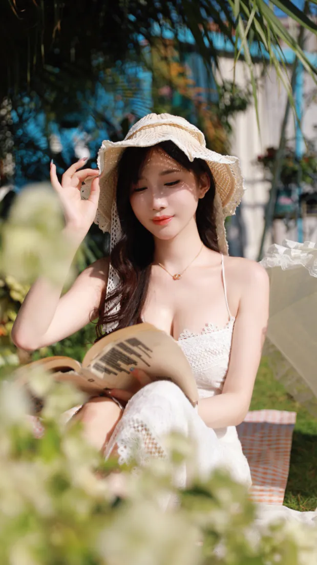 戴遮阳帽的白衣少女坐在花园藤椅上，手持书本，前景虚化绿植环绕。