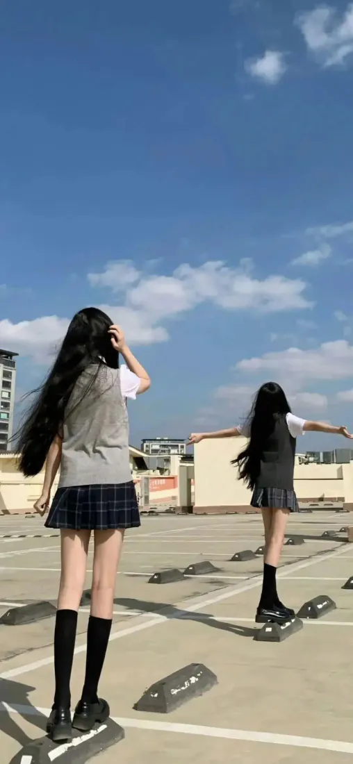 两名穿JK制服的长发少女背对镜头站在天台停车场，背景是晴朗蓝天与城市建筑。
